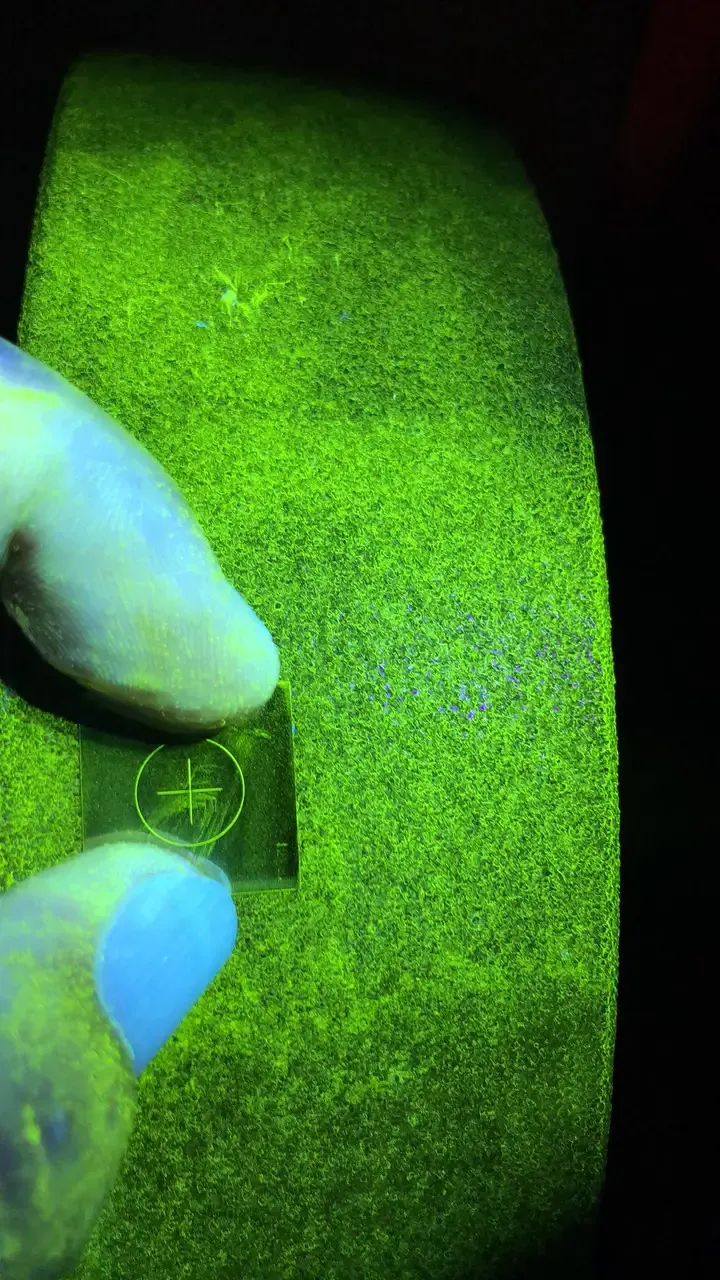A1 test piece held on a part, its circle and cross indications clearly visible under UV-A light