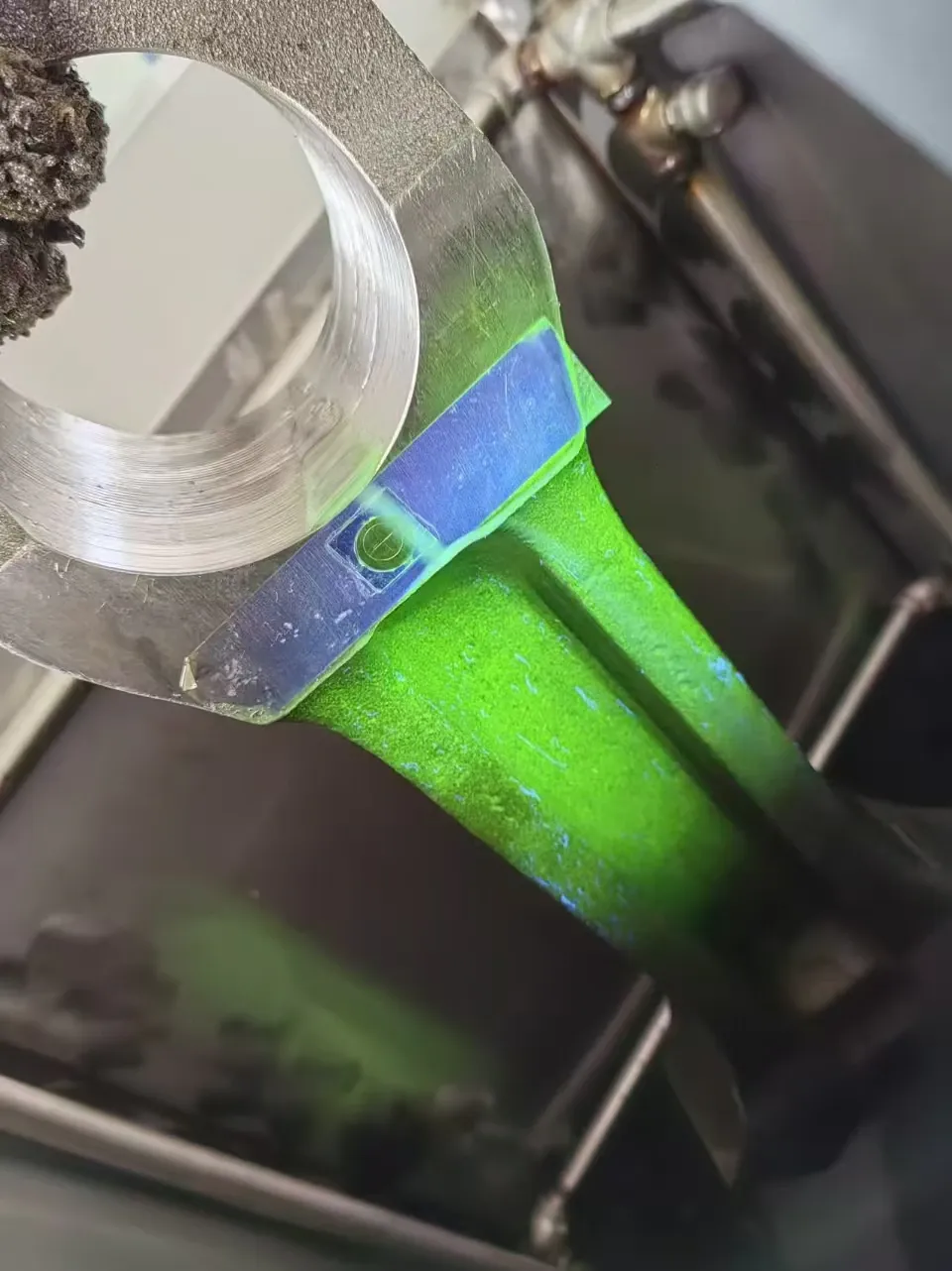Connecting rod coated with fluorescent magnetic suspension under UV-A light, a test piece on its shank