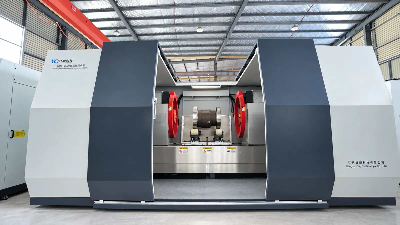 CQE-15000 magnetic particle inspection machine with its doors open, a part on the support rollers between two magnetizing coils