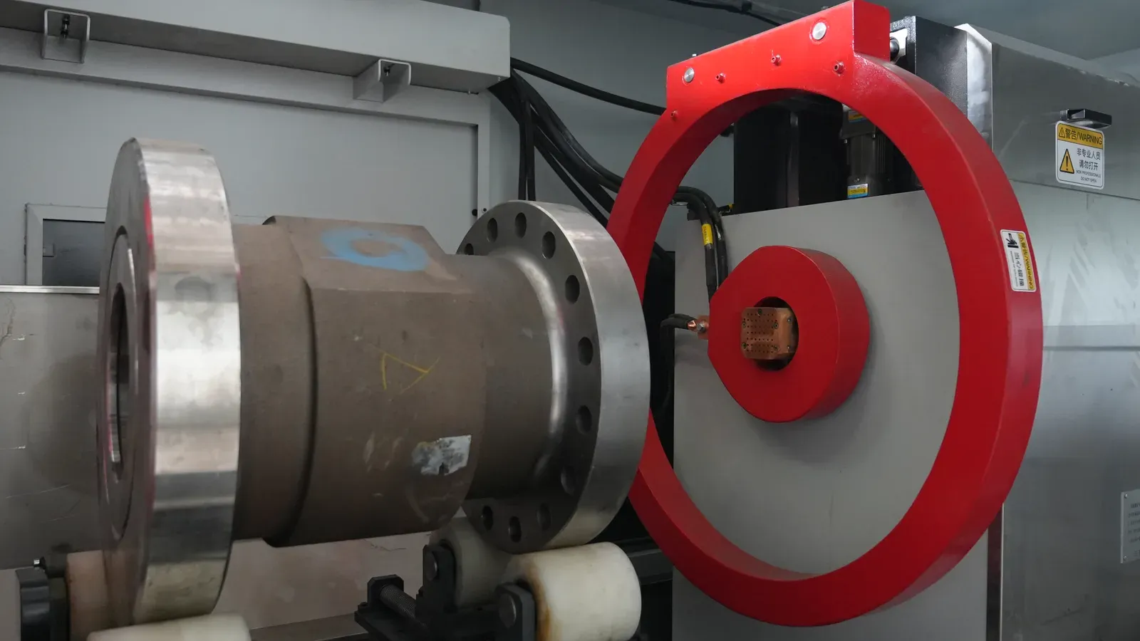 Flanged wellhead part on support rollers beside a magnetizing coil and electrode in the CQE-15000