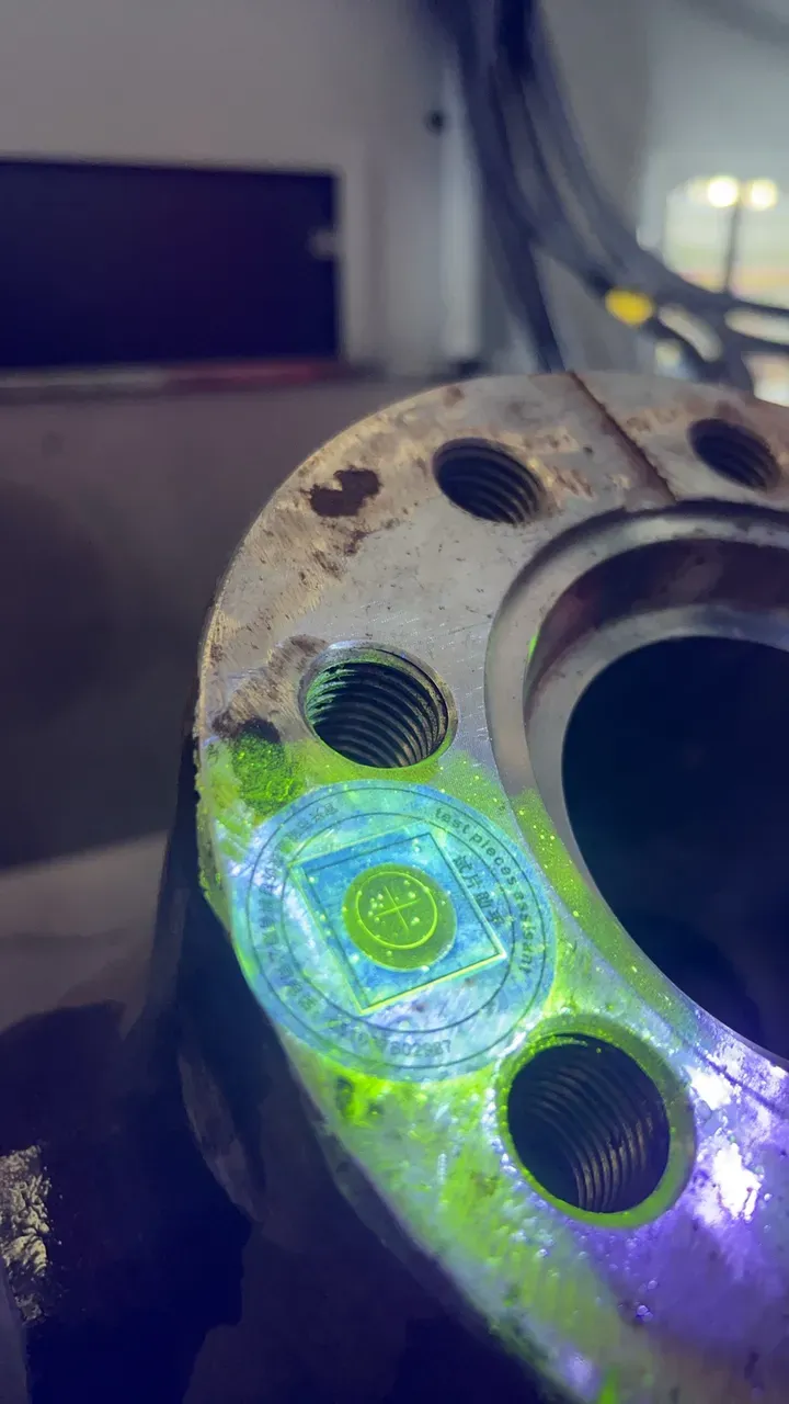 Test piece on a flange face, its cross indication glowing under UV-A light
