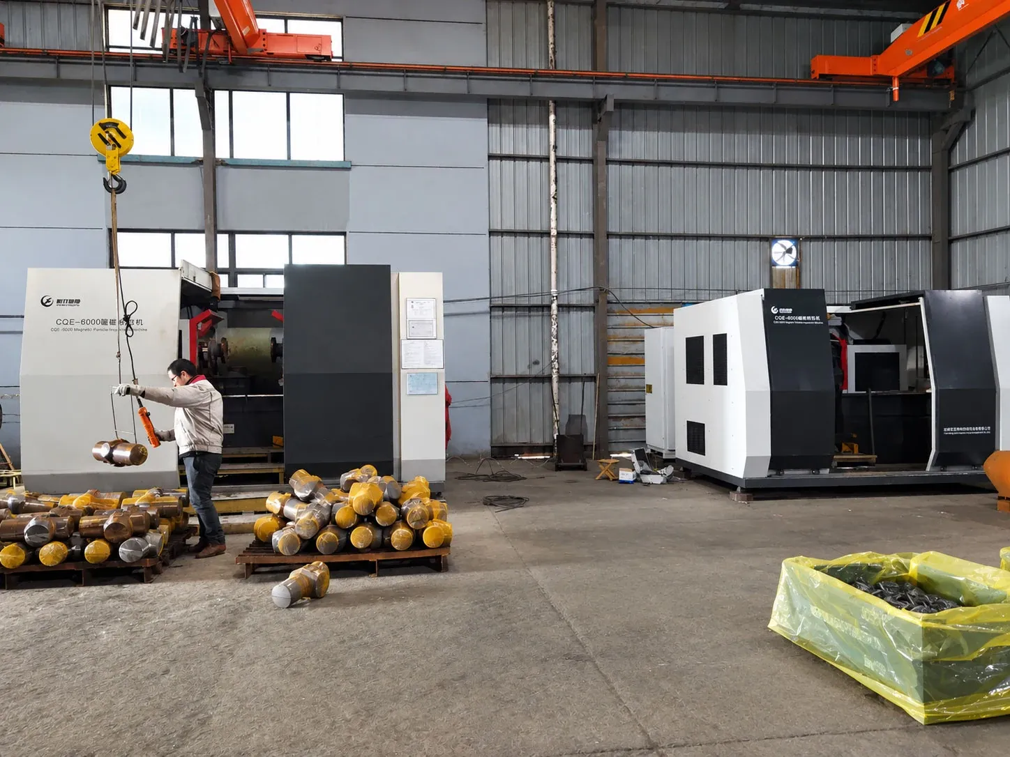 Two CQE-6000 machines in a workshop, with an operator lifting forged blanks from pallets